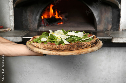 Professional chef holding tasty Italian pizza near oven in restaurant, closeup