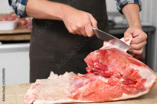 Butcher cutting fresh raw meat on counter in shop, closeup