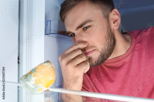 Man smelling stinky stale cheese in refrigerator