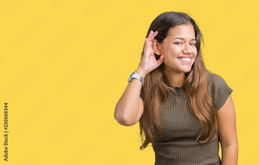 Young beautiful brunette woman over isolated background smiling with hand over ear listening an hearing to rumor or gossip. Deafness concept. Young beautiful brunette woman over isolated background smiling with hand over ear listening an hearing to rumor or gossip. Deafness concept.