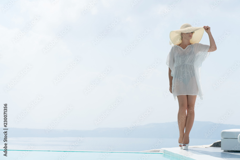 attractive girl in tunic and wide-brimmed hat posing near the pool