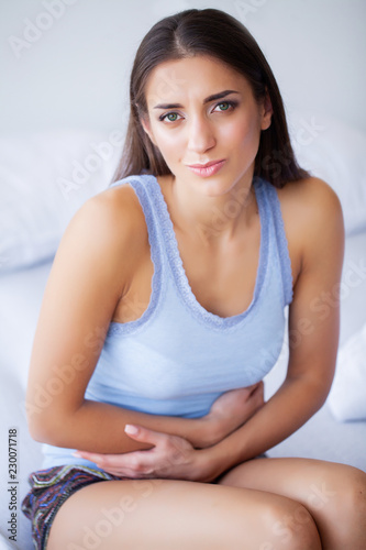 Stomach Pain. Unhealthy young woman with stomachache leaning on the bed at home