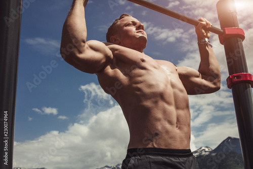 Obraz na plátně Caucasian male athlete with fit torso and strong hands doing chin ups outdoor