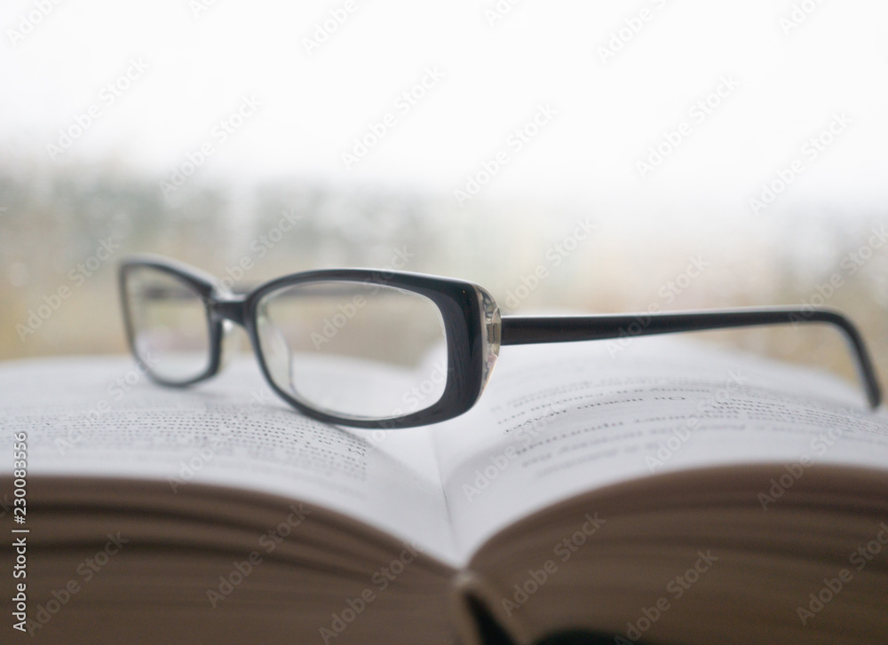 Eyeglasses on an open book with window on background in rainy weather Eyeglasses on an open book with window on background in rainy weather
