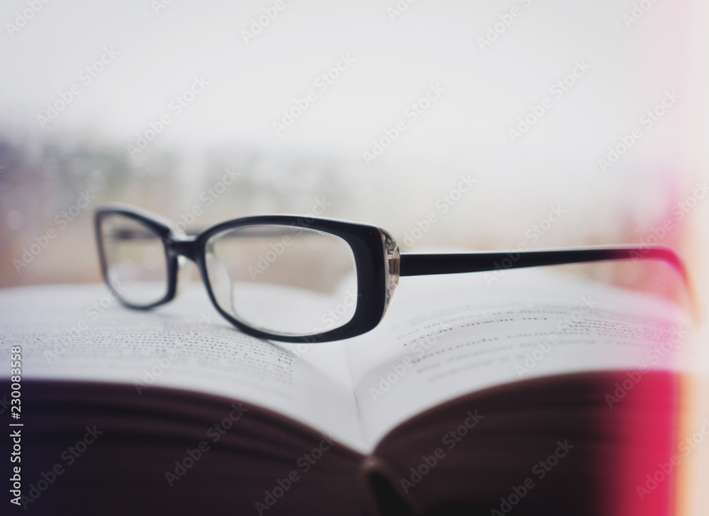 Eyeglasses on an open book with window on background in rainy weather Eyeglasses on an open book with window on background in rainy weather