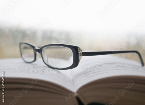 Eyeglasses on an open book with window on background in rainy weather