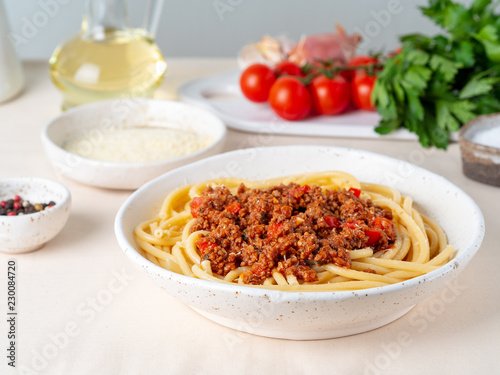pasta bolognese with tomato sauce, ground minced beef, basil leaves on white table, linen napkin, side view