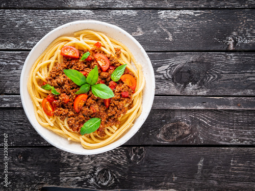 pasta bolognese with tomato sauce, ground minced beef, basil leaves on dark rustic wooden table, top view, copy space