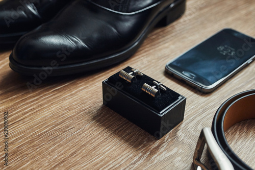 Different men's accessories such as: shoes, belt, cufflinks and telephone - are on the table