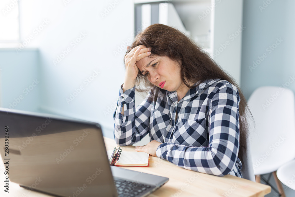 Technology, business and people concept - Young puzzled woman with the hand near the forehead sitting in front of laptop Technology, business and people concept - Young puzzled woman with the hand near the forehead sitting in front of laptop