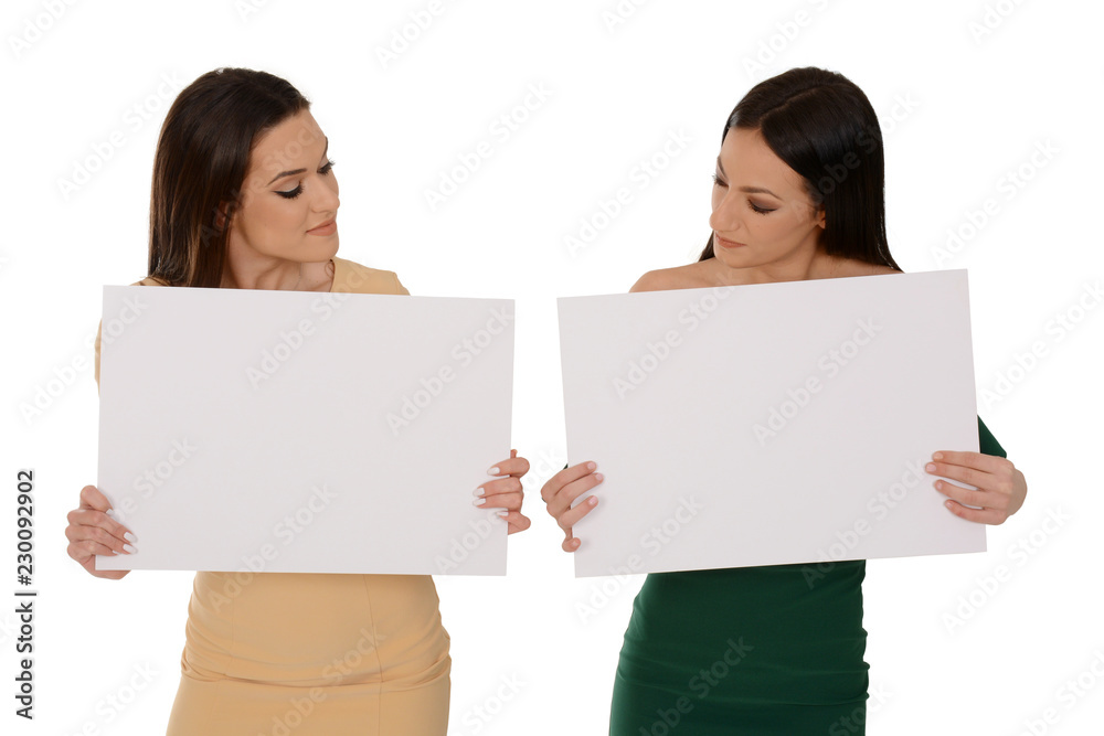 Two young smiling women holding two pieces of blank paper, looking down on papers Two young smiling women holding two pieces of blank paper, looking down on papers