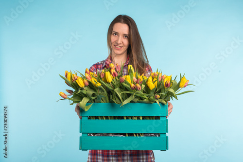 Happy caucasian female florist laughing and holding big box of tulips on blue background