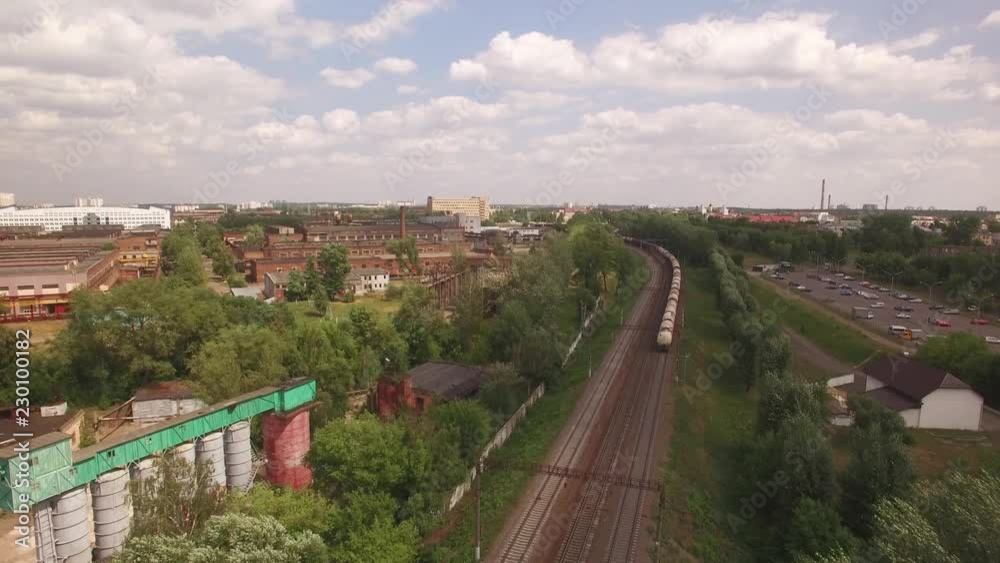 Electric freight train, locomotive moves rides by rail with wagons, transportation, deliver barrel, petrol, oil tank, transports cargo in city, town. Aerial view, drone, air shoot Electric freight train, locomotive moves rides by rail with wagons, transportation, deliver barrel, petrol, oil tank, transports cargo in city, town. Aerial view, drone, air shoot