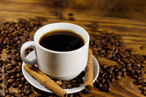 Cup of coffee  roasted coffee beans and cinnamon sticks on wooden table