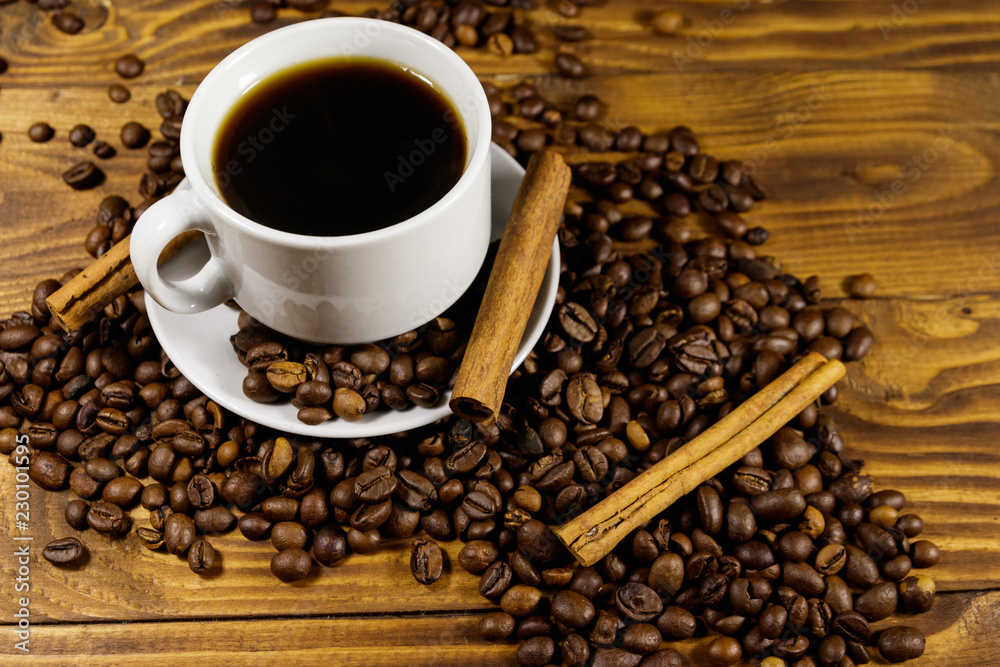 Cup of coffee, roasted coffee beans and cinnamon sticks on wooden table Cup of coffee, roasted coffee beans and cinnamon sticks on wooden table