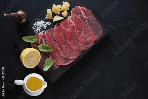 Carpaccio made of raw marbled beef over black stone background, high angle view, horizontal shot with copyspace