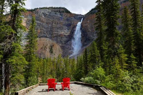 Two red chairs at a bottom of Takakkaw falls on a sunny afternoon. Takakkaw Falls is a waterfall located in Yoho National Park, near Field, British Columbia in Canada. photo