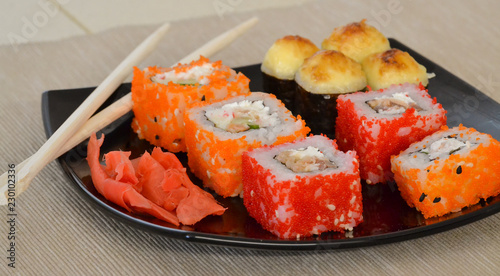 Sushi and rolls on a black plate with chopsticks.