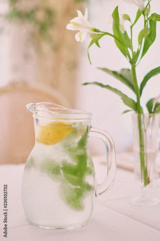 Fototapeta premium Glass jug of cold lemonade on a light background cafe. Pitcher lemon water with mint. Cold lemonade box