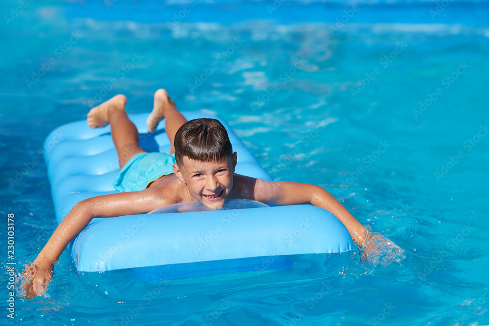 Boy relaxing on inflatable mattress at hotel swimming pool in summer. He is smiling and looking into camera.