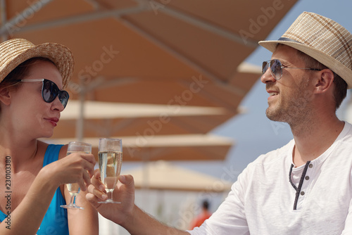 Young European couple is sitting at the pool bar and enjoying their vacations. They are celebrating something and drinking champagne.