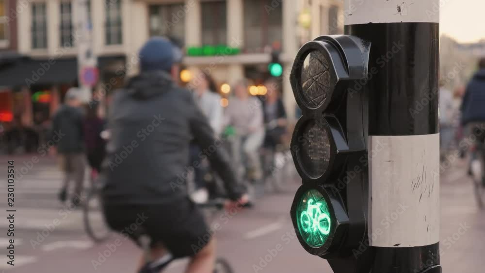 Many bicycles ride on Amsterdam street, in the foreground a special traffic light for cyclists. Environmentally friendly mode of transport