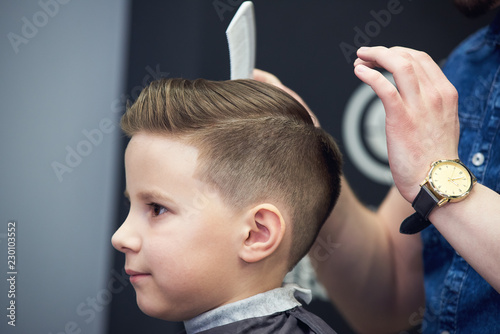 Barber shop. Barber makes hairstyle to a boy with styling gel and hairbrush.
