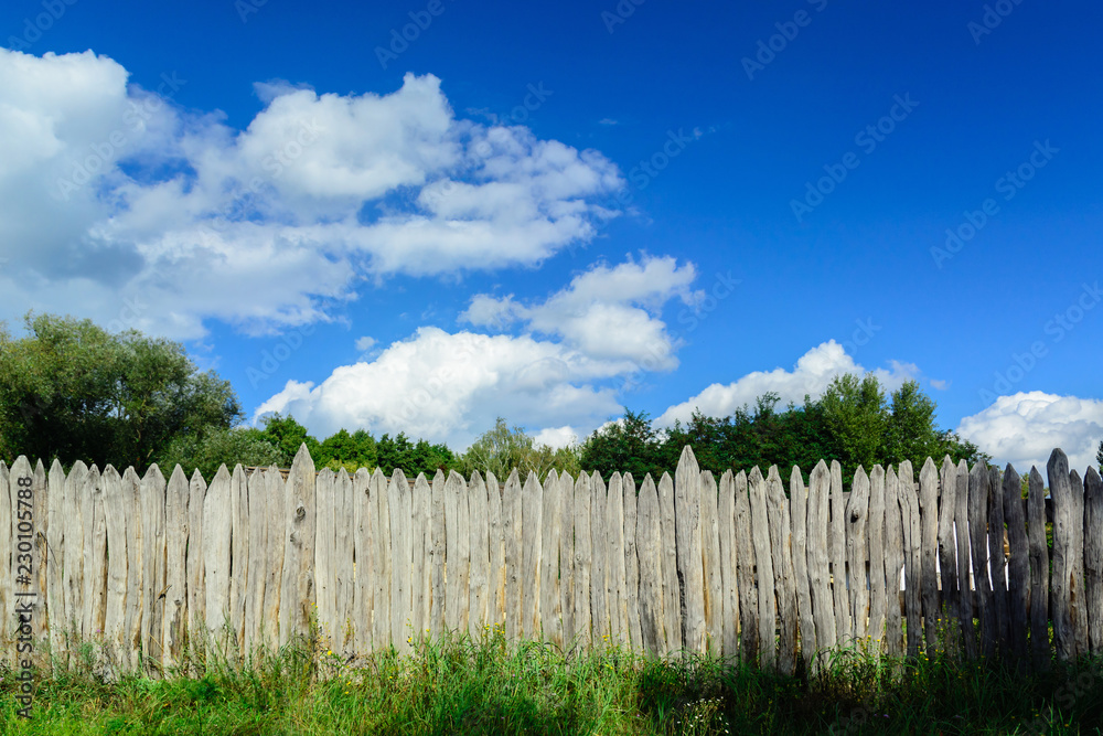 An old log fence and a blue sky with clouds. Security and fencing. Protection against thieves