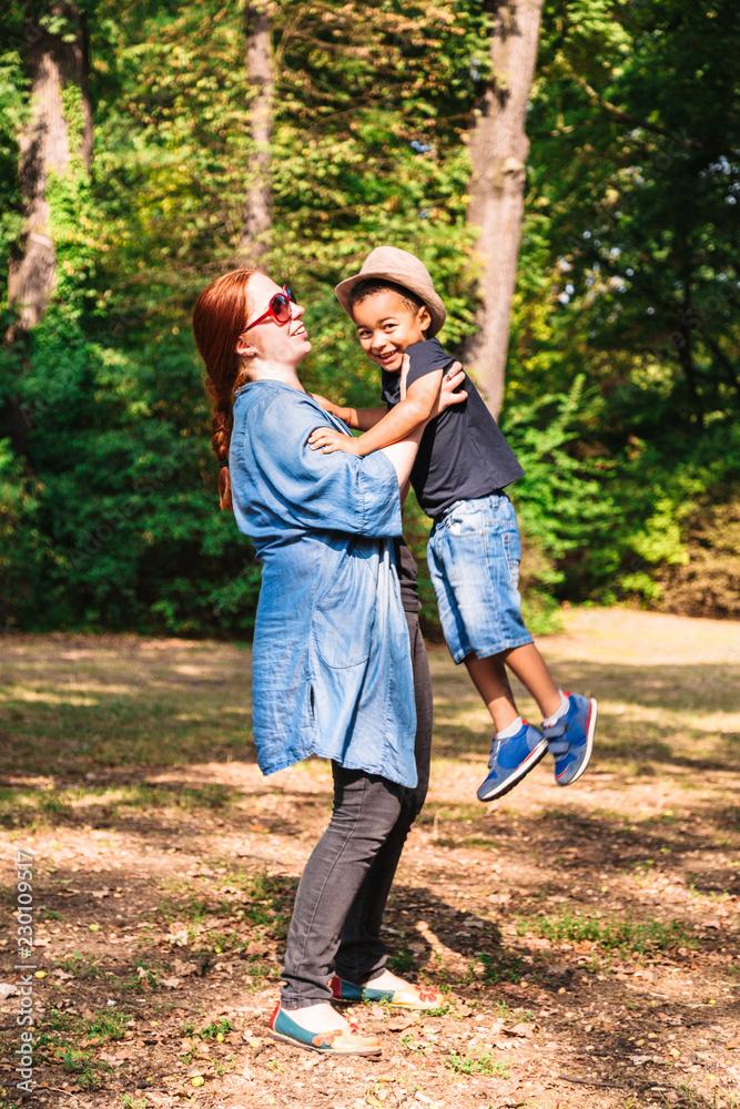 Fototapeta premium Mother holds and lifts up her son for fun in park