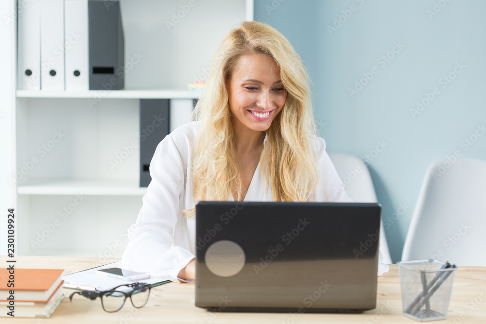 Working, business, technology and people concept - young blonde woman watching something in screen of laptop and smiling Working, business, technology and people concept - young blonde woman watching something in screen of laptop and smiling