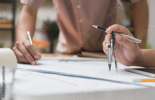 Hands of architect or engineer using drawing compass with blueprint on desk in office.Team of architects engineer discussing and check documents and business workflow.Construction concept.