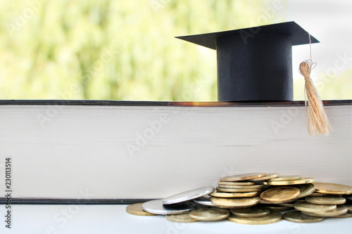 Graduation card for saving coins for scholarships for conceptual financing and education. Graduation microcline and gold coins near a book on a green background, concept of investment education, closi photo