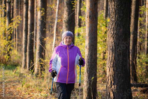 A woman over the age of 65 is engaged in Nordic walking in the fresh air. © Sergei Malkov