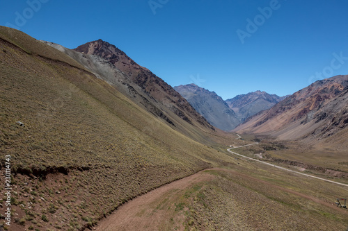 Narrow road in a valley surrounded by the Andes Mountain Range under blue sky in Mendoza Argentina