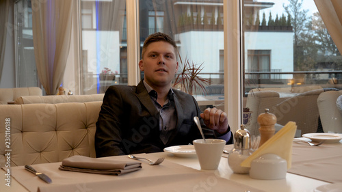 The waiter in a beautiful restaurant brings a young man (man) a cup of coffee (tea). Concept from: Beautiful Restaurant, Coffee, Tea, Drinks, Business Man, Waiter. photo