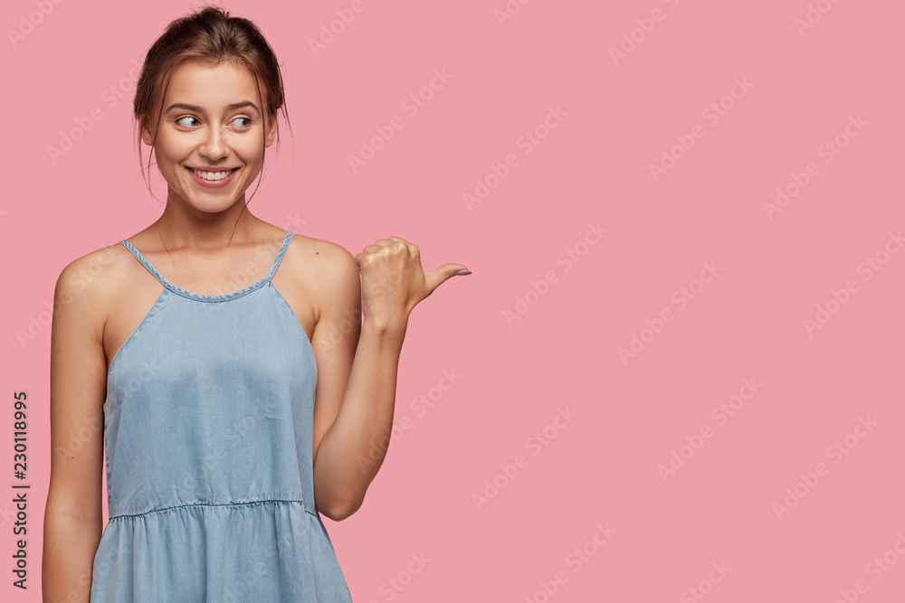 Studio shot of pleased European woman with joyful expression, enjoys watching cool performance, dressed in fashionable dress, isolated over pink background. Advertisement and promotion concept Studio shot of pleased European woman with joyful expression, enjoys watching cool performance, dressed in fashionable dress, isolated over pink background. Advertisement and promotion concept