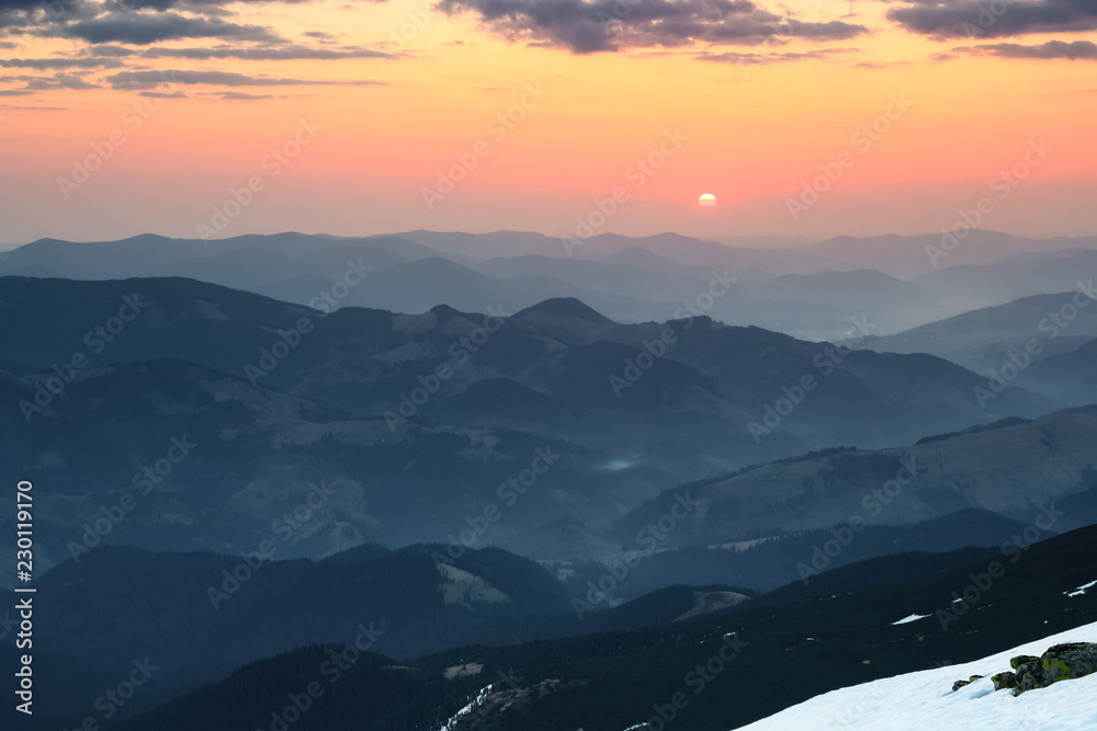 From the snow covered  meadow opens a panoramic view of the mountains, illuminated by the morning sun rays. Sunrise. Sky with clouds.