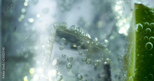 Close-up of a refreshing drink with bubbles interacting with ice and lime.