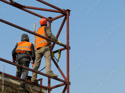 Construction workers working on scaffolding. Welders on the construction site against the clear blue sky