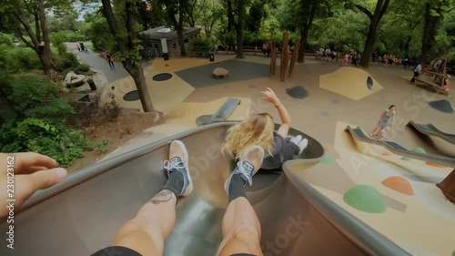 Young couple or teenage friends, pov shot going down metal kids or playground slide at park during summer vacation, fun and unconventional activity for weekend or date, laugh and smile photo