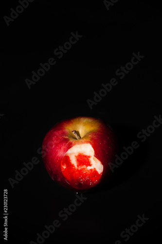 An apple with a bloody bite mark on a black background