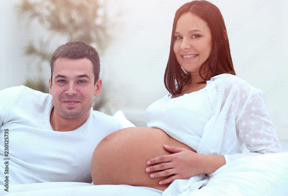 Laughing caucasian pregnant woman lying on bed with her husband in the bedroom Laughing caucasian pregnant woman lying on bed with her husband in the bedroom