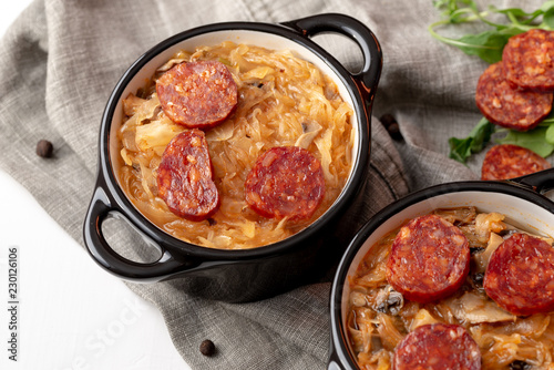 Slovak Christmas cabbage soup in two small pots with sausage on the top on white background.