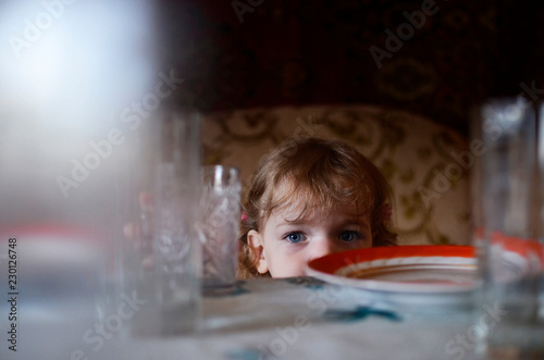 A girl looks out from behind a table