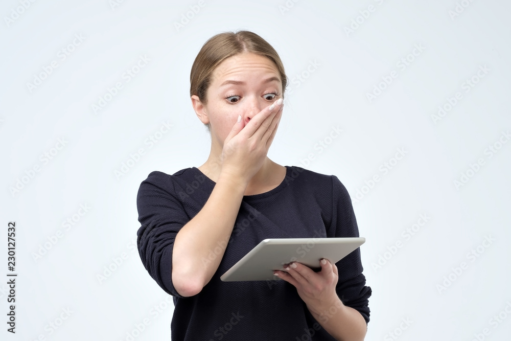 Shocked woman looking at digital tablet with surprise and shock over gray background. Astonishment or hot news in internet Shocked woman looking at digital tablet with surprise and shock over gray background. Astonishment or hot news in internet
