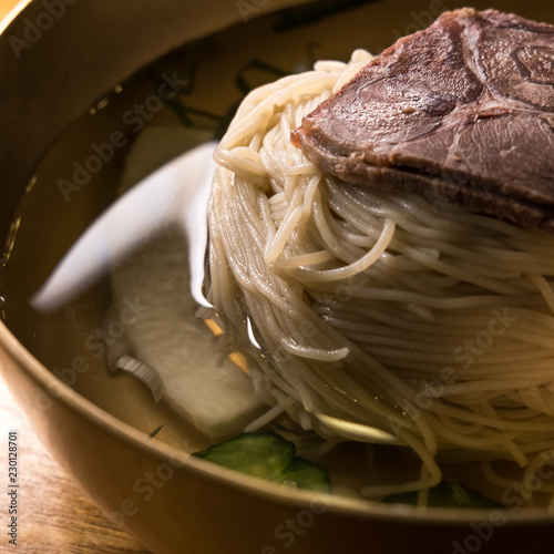 Naengmyeon (Korean cold noodles) in a ice beef broth. Garnished with thinly sliced pear, beef, and cucumber and served with half of a hard boiled egg. Typically enjoyed with vinegar and spicy mustard. photo