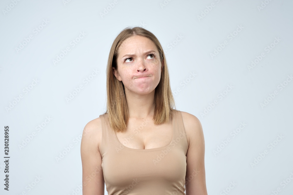 Indoor shot of cute girl looking away, having doubtful and indecisive face expression, pursuing her lips as if forbidden to say anything. Indoor shot of cute girl looking away, having doubtful and indecisive face expression, pursuing her lips as if forbidden to say anything.
