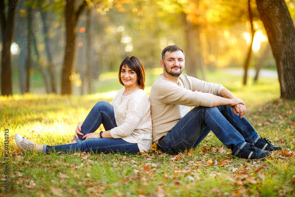 Young family and autumn concept. Couple in love sits on fallen leaves in park. Girl and bearded guy or happy lovers on a date. Man and woman with cheerful faces on grass and leaves background Young family and autumn concept. Couple in love sits on fallen leaves in park. Girl and bearded guy or happy lovers on a date. Man and woman with cheerful faces on grass and leaves background