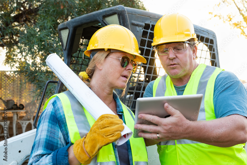 Male and Female Workers With Technical Blueprints and Computer Tablet Talking at Construction Site Male and Female Workers With Technical Blueprints and Computer Tablet Talking at Construction Site