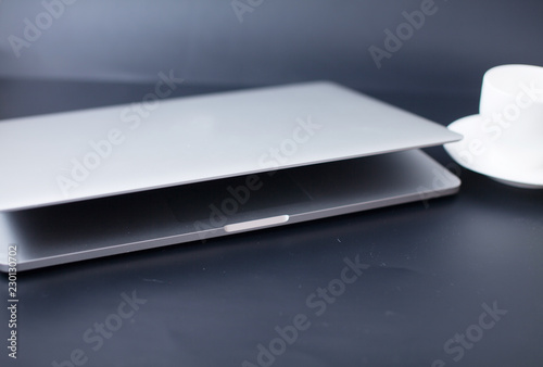 Silver laptop half closed on dark background with cup of coffee near